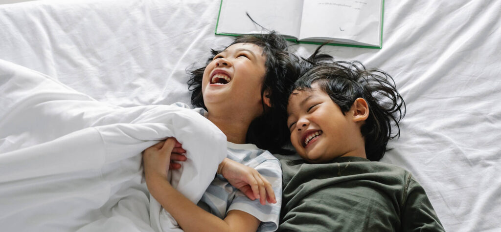 two kids laying in bed laughing with a book